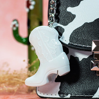 White cowboy boot keychain attached to a black and white patterned bag.