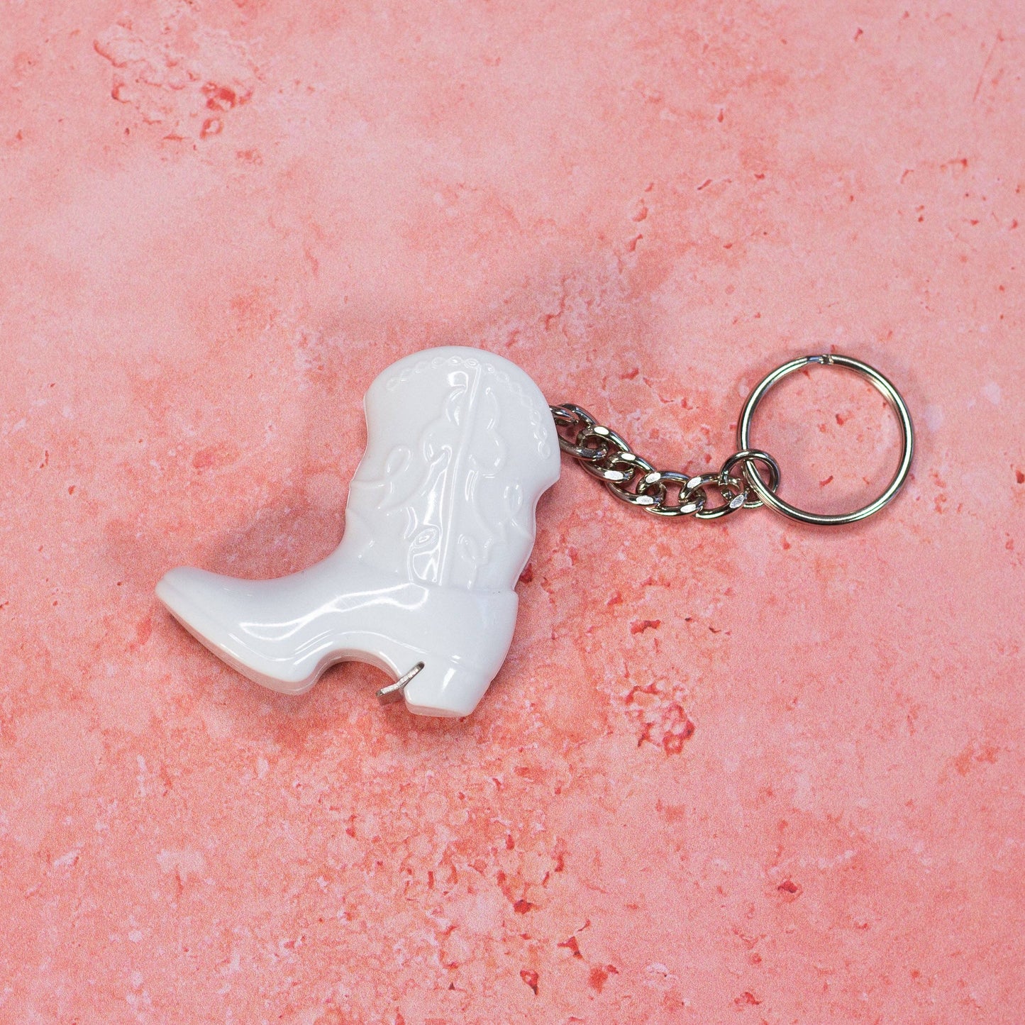 White cowboy boot keychain on a pink textured background