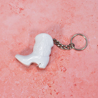 White cowboy boot keychain on a pink textured background
